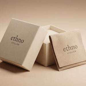 May include: An open, off-white box with the text "ethno ATELIER" printed on the lid. A matching pouch with the same text rests beside the box. The background is a soft, neutral color.