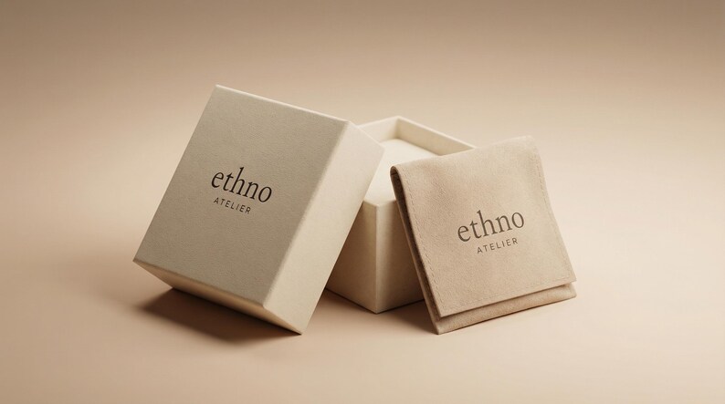May include: An open, off-white box with the text "ethno ATELIER" printed on the lid. A matching pouch with the same text rests beside the box. The background is a soft, neutral color.