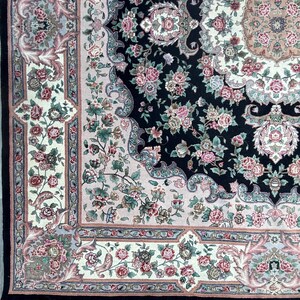 May include: Close-up of an ornate area rug with a black central field. The rug features a floral pattern in shades of pink, green, and cream, with a detailed border and fringe. The design includes roses and other stylized flowers.