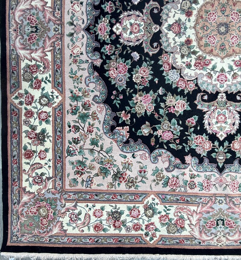May include: Close-up of an ornate area rug with a black central field. The rug features a floral pattern in shades of pink, green, and cream, with a detailed border and fringe. The design includes roses and other stylized flowers.