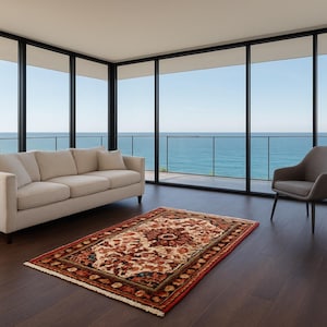 May include: A living room with a beige sofa, a gray armchair, and a patterned rug. The room has large windows overlooking the ocean. A potted plant sits near the sofa.
