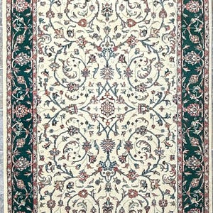 May include: Rectangular ivory rug with a detailed floral pattern in shades of red, blue, and green. The rug has a dark green border with floral motifs and a cream-colored fringe.