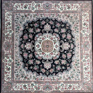 May include: Square area rug with a central black medallion design, surrounded by floral patterns in pink, cream, and green. The rug has a black border and fringe.