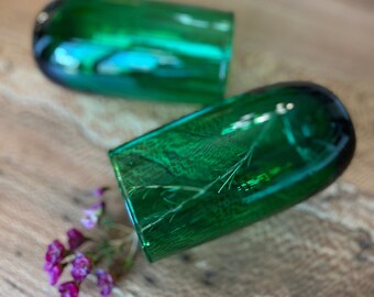 May include: Two green glass tumblers with a textured design. The tumblers are empty and sitting on a wooden surface.