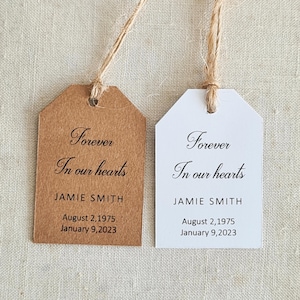May include: Two gift tags with twine, one brown and one white. The tags read "Forever In our hearts" with the name "JAMIE SMITH" and dates "August 2,1975" and "January 9,2023".