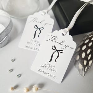 May include: Two white thank you gift tags with black ribbon bows and the text "Thank you" and "Faye's Hen Party 28th March 2025".