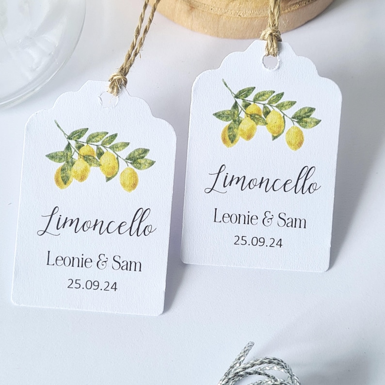 May include: Two white gift tags with a watercolor illustration of a lemon branch. The tags are tied with twine and have the text "Limoncello" and "Leonie & Sam 25.09.24" printed on them.