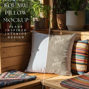 Könnte beinhalten: Ein quadratischer Kissen-Mockup mit einem von Pflanzen inspirierten Design, mit weißem Hintergrund und beigem Blumenmuster. Die Szene umfasst weitere Kissen, Pflanzen in Töpfen und den Text "SQUARE PILLOW MOCKUP PLANT INSPIRED INTERIOR DESIGN."