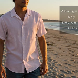 Pu&ograve; includere: Una camicia rosa chiaro a maniche corte con colletto a campana. La camicia &egrave; abbottonata e il testo "Change to Any Design or Color" &egrave; in una casella sullo sfondo. La persona &egrave; in piedi su una spiaggia sabbiosa con l'oceano sullo sfondo.
