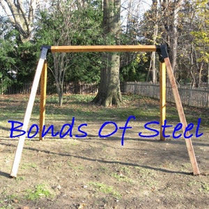 May include: A wooden swing set with black metal brackets. The swing set is in a grassy backyard with a wooden fence in the background. The text "Bonds of Steel" is written in blue on the ground in front of the swing set.