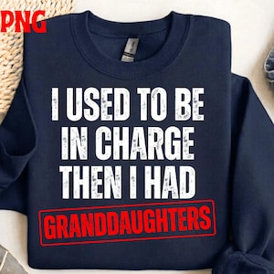 Può includere: Felpa blu navy con testo bianco: "I USED TO BE IN CHARGE THEN I HAD GRANDDAUGHTERS". La parola "GRANDDAUGHTERS" è in un rettangolo rosso. Il testo è in grassetto, senza grazie.