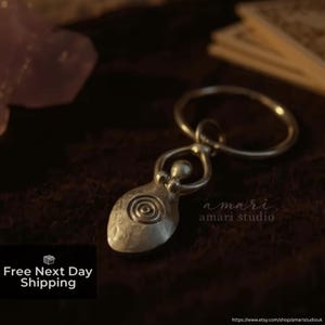 May include: A silver pendant depicting a stylized female form with a spiral motif. The pendant is connected to a circular ring. The image also includes the text "amari studio".