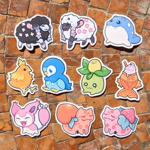 May include: A collection of colorful, die-cut stickers featuring various cartoon characters and creatures. The stickers include a black sheep, a white sheep with pink flowers, a blue seal, a yellow chick, a blue penguin, a green plant, and a fish-shaped dessert.