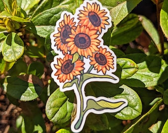May include: A sticker featuring a cluster of sunflowers with orange petals and dark brown centers. The sunflowers are arranged on a green stem with a white border, set against a backdrop of green leaves.