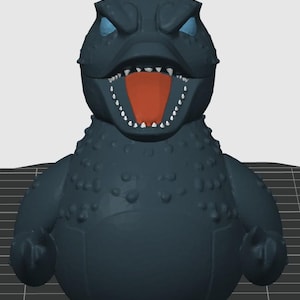 May include: A dark teal Godzilla-like figure with an open mouth revealing an orange interior and white teeth. The figure has blue eyes and a textured body. A small fin is on top of the head.