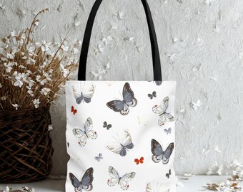 May include: White tote bag with a black handle. The bag is patterned with watercolour butterflies in grey, blue, and red. The butterflies are of different sizes and are scattered across the bag's surface. The bag is made of a sturdy material.
