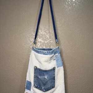 Peut inclure: Un sac fourre-tout fait à la main à partir de denim recyclé et de tissu blanc. Le sac présente une poche en jean, des patchs et une étiquette Levi Strauss & Co. Les sangles sont en denim bleu foncé.