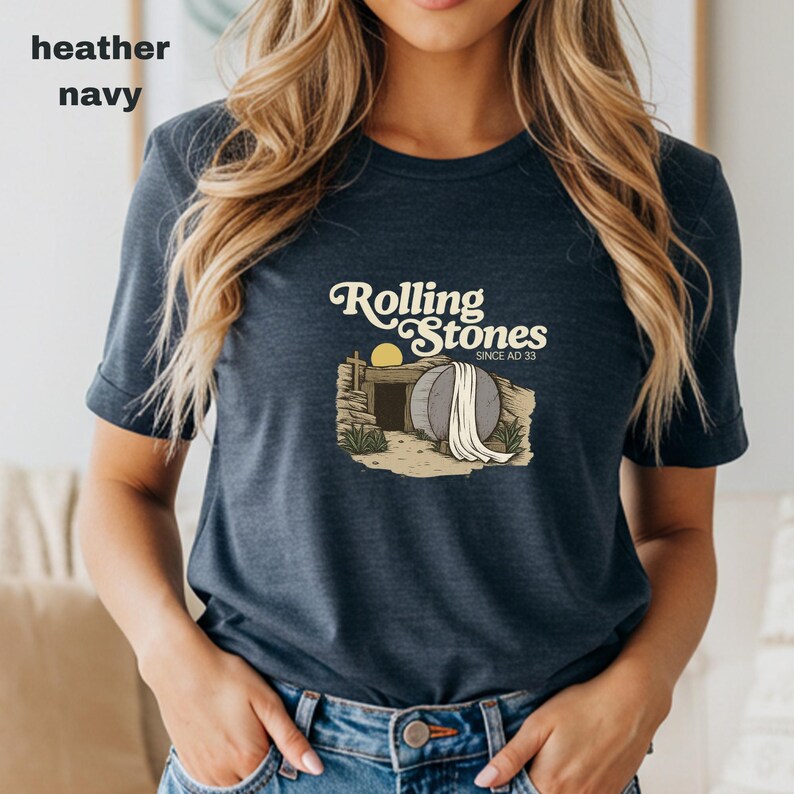 May include: Heather navy t-shirt with the text "Rolling Stones Since AD 33" above an illustration of an open tomb with a stone and a cross. The shirt is a dark blue color.
