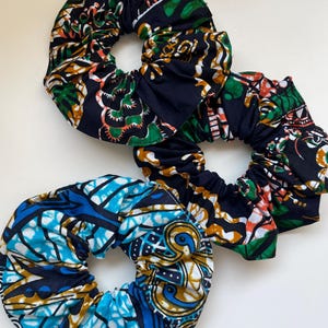 Puede incluir: Primer plano de tres coleteros coloridos. Uno es azul y blanco, los otros son negros con diseños verdes, naranjas y blancos. Estos accesorios para el cabello son perfectos para añadir un toque de color a cualquier peinado.