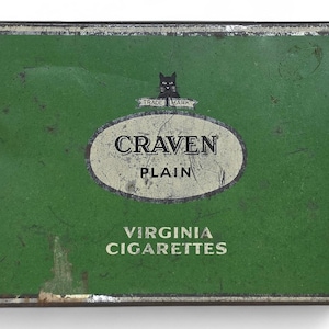 May include: A vintage Craven Plain Virginia Cigarettes tin. The rectangular tin has a green background with a white oval in the center. The oval contains the words "CRAVEN PLAIN". A black cat is above the oval. The words "VIRGINIA CIGARETTES" are at the bottom.