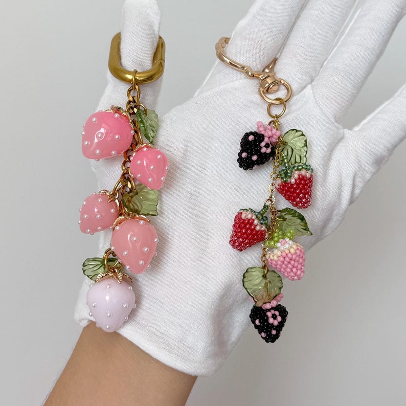 Pu&ograve; includere: Due portachiavi a fragola con perline. Uno presenta fragole rosa con pois bianchi e foglie verdi, l'altro ha bacche di perline rosse, rosa e nere con foglie verdi. Entrambi hanno hardware color oro.