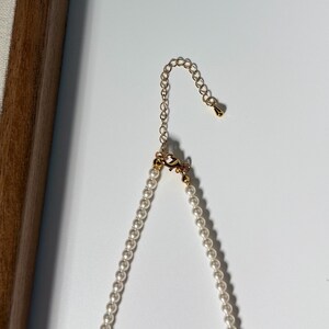 Peut inclure: Un collier de perles d&eacute;licat avec une cha&icirc;ne et un fermoir dor&eacute;s. Le collier est compos&eacute; de petites perles blanches rondes. La cha&icirc;ne dor&eacute;e s'&eacute;tend sur une longueur r&eacute;glable, et le fermoir est visible en haut de l'image.