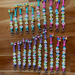 May include: A collection of personalised keychains featuring colourful plastic letter beads spelling names like Liri, Leah, Besa, Rene, Opal, Harley, Nancy, Addey, Emily, Grace, Jess, Mira, Ciara, Aviva, Kaitlyn, Juliette, Stephanie, Shachar, Gidget, and Shauna.