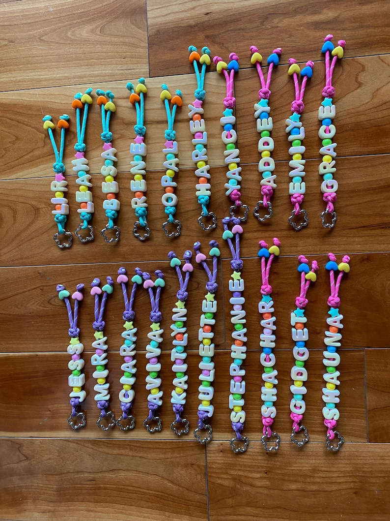 May include: A collection of personalised keychains featuring colourful plastic letter beads spelling names like Liri, Leah, Besa, Rene, Opal, Harley, Nancy, Addey, Emily, Grace, Jess, Mira, Ciara, Aviva, Kaitlyn, Juliette, Stephanie, Shachar, Gidget, and Shauna.