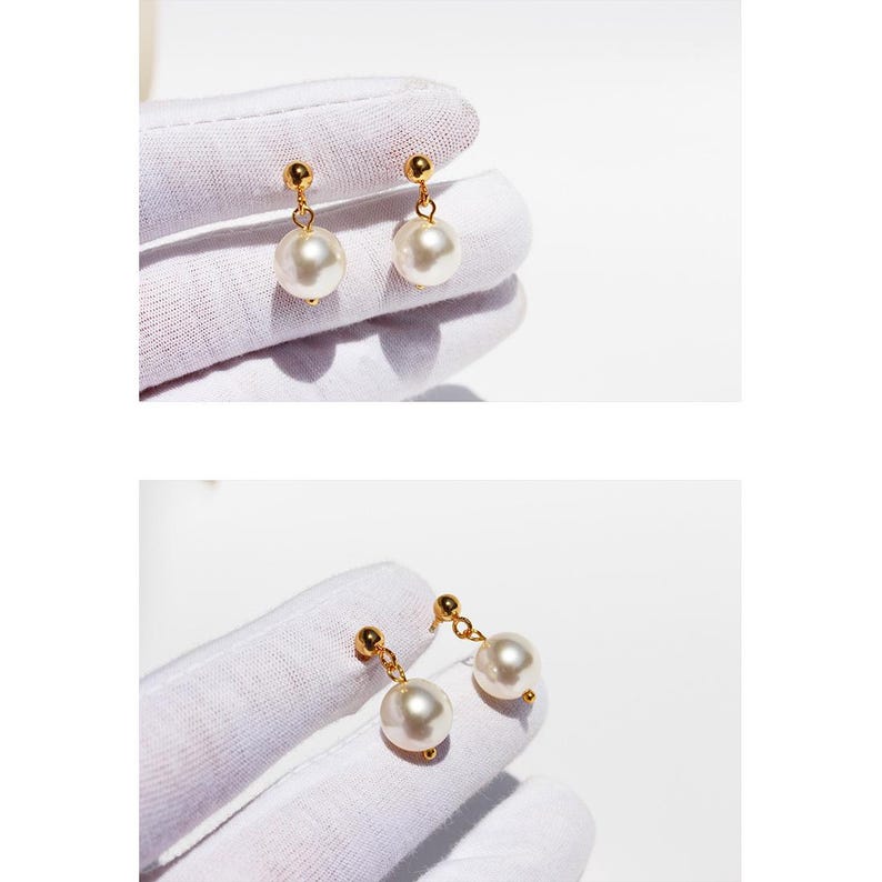 Peut inclure: Une paire de boucles d'oreilles pendantes dor&eacute;es avec de grosses perles blanches rondes. Les boucles d'oreilles ont un design simple avec une petite boule dor&eacute;e en haut et une perle suspendue en dessous. Le fond est blanc.