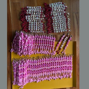 May include: A collection of beaded keychains featuring white letter beads spelling ALABAMA on red cords, and pink letter beads spelling TAMPA or LONDON on pink cords, all attached to gold-toned metal clasps with flower-shaped accents.