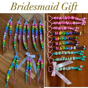 May include: A collection of personalised keychains featuring colourful plastic letter beads spelling names like Mallory, Hannah, Haley, Megan, Linzy, Serena, Natalie, and Ashley, attached to heart-shaped clasps with some accented by polka-dot ribbons.