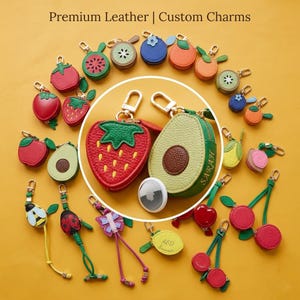 Puede incluir: Una colección de llaveros de cuero coloridos con diseños de frutas e insectos, incluyendo fresas, aguacates, cerezas y una mariquita. Los llaveros se muestran sobre un fondo amarillo. El texto en la parte superior dice "Premium Leather | Custom Charms."
