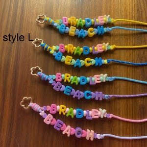May include: Four beaded lanyards labelled style L, each featuring colourful plastic letter beads spelling BRADLEY BEACH. The lanyards use various cord colours including yellow, blue, purple, and pink, and each ends with a gold-toned flower-shaped clasp.