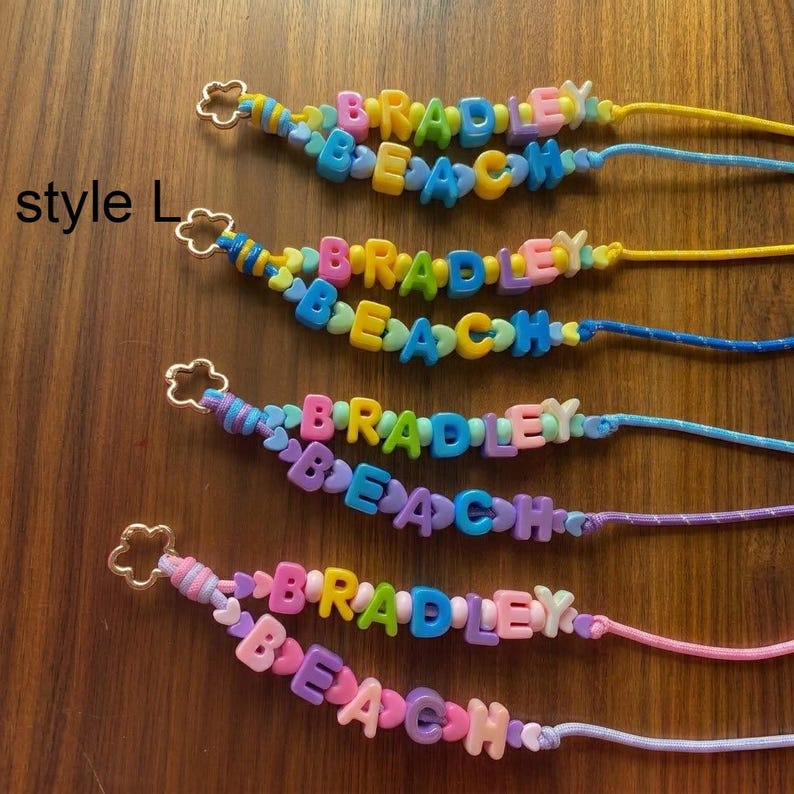 May include: Four beaded lanyards labelled style L, each featuring colourful plastic letter beads spelling BRADLEY BEACH. The lanyards use various cord colours including yellow, blue, purple, and pink, and each ends with a gold-toned flower-shaped clasp.