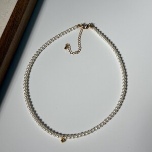 Peut inclure: Un d&eacute;licat collier de perles avec un fermoir dor&eacute; et un petit charme dor&eacute;. Le collier est compos&eacute; de nombreuses petites perles blanches rondes. Le design est simple et &eacute;l&eacute;gant, adapt&eacute; &agrave; diverses occasions.