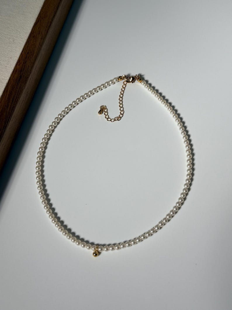 Peut inclure: Un d&eacute;licat collier de perles avec un fermoir dor&eacute; et un petit charme dor&eacute;. Le collier est compos&eacute; de nombreuses petites perles blanches rondes. Le design est simple et &eacute;l&eacute;gant, adapt&eacute; &agrave; diverses occasions.