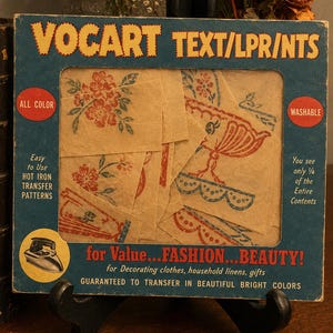 May include: Vintage Vocart Text/LPR/NTS iron-on transfer patterns. The blue box features the text "VOCART TEXT/LPR/NTS" in yellow, with red and blue floral designs visible through a window. The box promises "Value...FASHION...BEAUTY!" for decorating clothes and linens.