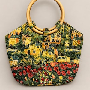 Peut inclure: Sac fourre-tout matelassé avec une poignée en bois. Le sac présente un imprimé coloré d'une scène de village dans la partie supérieure et un motif floral en bas. La poignée du sac est en bois clair.