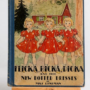 May include: A vintage children's book cover with three girls in red polka dot dresses. The title reads "Flicka, Ricka, Dicka and the New Dotted Dresses" by Maj Lindman. The background depicts a red house and a green landscape.