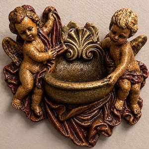 Puede incluir: Un lavabo decorativo de querubines montado en la pared. Dos figuras de querubines con alas y pelo dorados sostienen una pila. La pila y los querubines están pintados en tonos dorados y marrones, con un acabado texturizado y agrietado. Los querubines están cubiertos con tela burdeos.