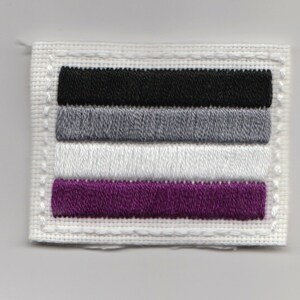 May include: A white fabric patch with a black, grey, white, and purple embroidered stripe pattern. The patch has a white stitched border.