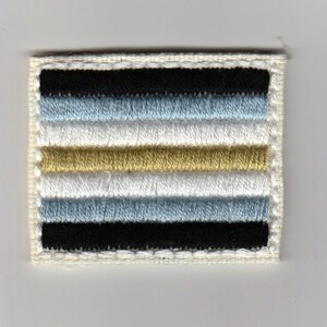 May include: A white patch with a black, light blue, white, gold, and light blue striped design. The patch is embroidered with a white border.
