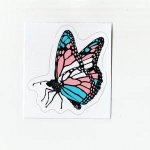 Puede incluir: Una pegatina de una mariposa con alas rosas, azules y blancas. La mariposa está en vuelo y tiene contornos negros.