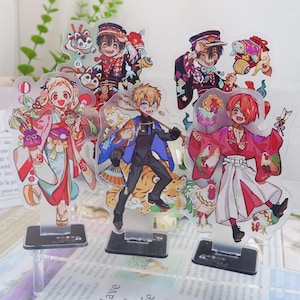 May include: A set of acrylic anime character standees. The figures depict colourful illustrations of anime characters in various poses, with detailed clothing and accessories. Each standee has a clear base for display.