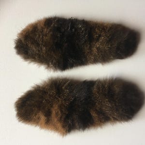 May include: Two brown and black faux fur tails. The tails are long and fluffy.