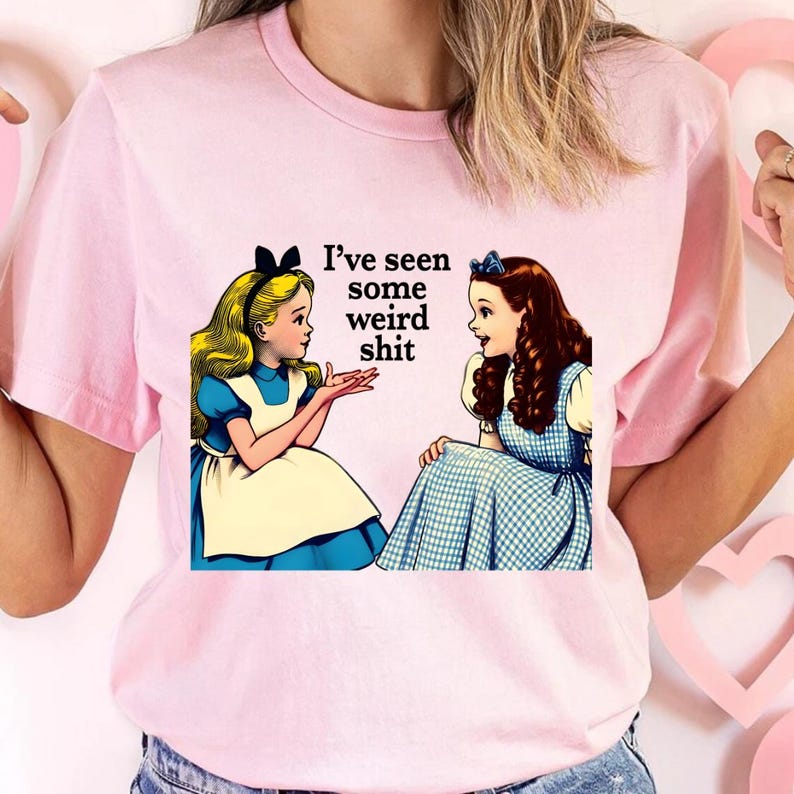 May include: Pink t-shirt featuring a graphic of two Alice in Wonderland characters with the text "I've seen some weird shit." The illustration depicts the characters in blue dresses and white aprons, with one blonde and one brunette.