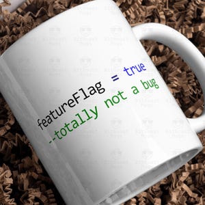 May include: White ceramic mug with the text "featureFlag = true --totally not a bug" in a programming font. The mug is inside a white box filled with brown crinkle paper.