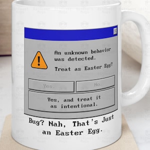 May include: White ceramic mug with a handle, featuring a humorous computer error message. The message reads "An unknown behavior was detected. Treat as Easter Egg?" with "Yes" and "No" options. Below, it says "Bug? Nah, That's Just an Easter Egg."
