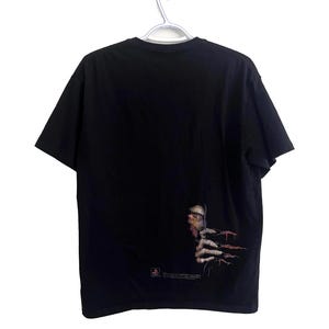May include: Black t-shirt with a graphic of a face and hand with long, sharp nails. The graphic is on the lower right side of the shirt. The shirt is hanging on a silver hanger.