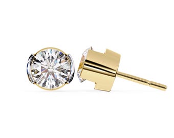 May include: A pair of gold stud earrings with a round, clear gemstone. The earrings have a bezel setting with a gold and silver-tone metal design. The post is gold.